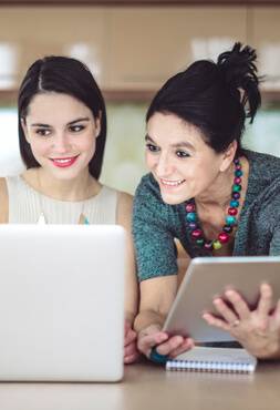 Adult woman and her mother review business notes on a tablet and laptop