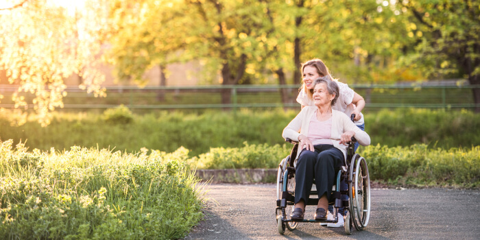 elder woman in wheelchair with assistant in the park at sunset