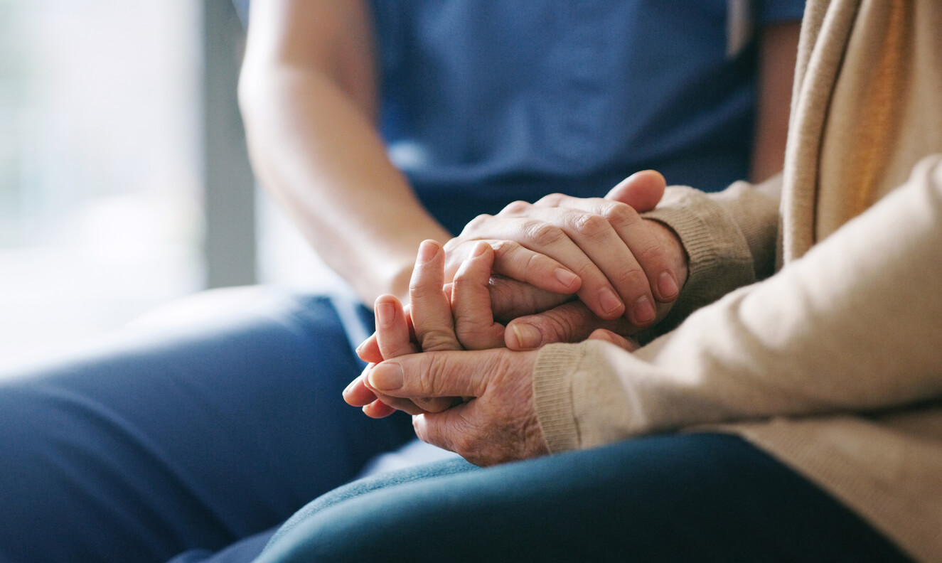Elderly woman holding a nurse's hand.