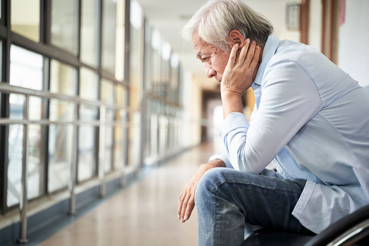 Elderly man thinking about his future in hospital hallway.