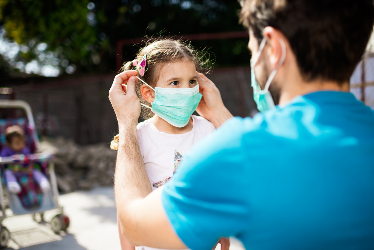 Father helping his daughter put on mask during COVID-19 pandemic.