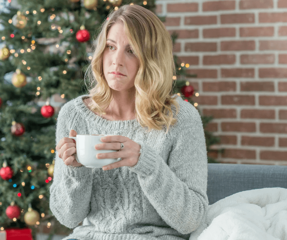 a sad woman holding a coffee cup in front of a Christmas tree