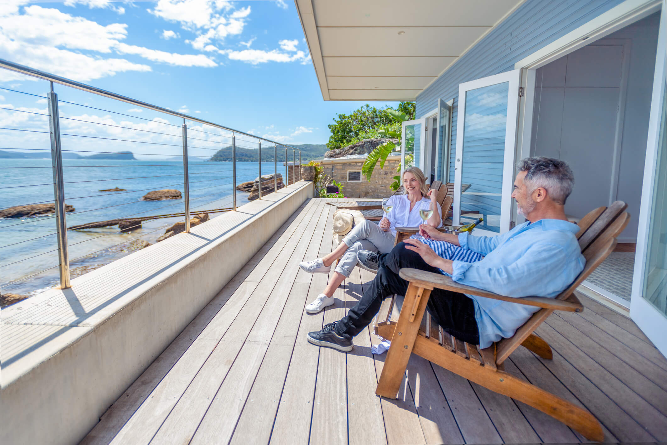 Middle aged couple drinking wine on deck of waterfront vacation home