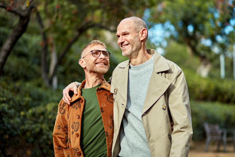 Waist up view of mature men dressed for autumn, arms around each other and smiling