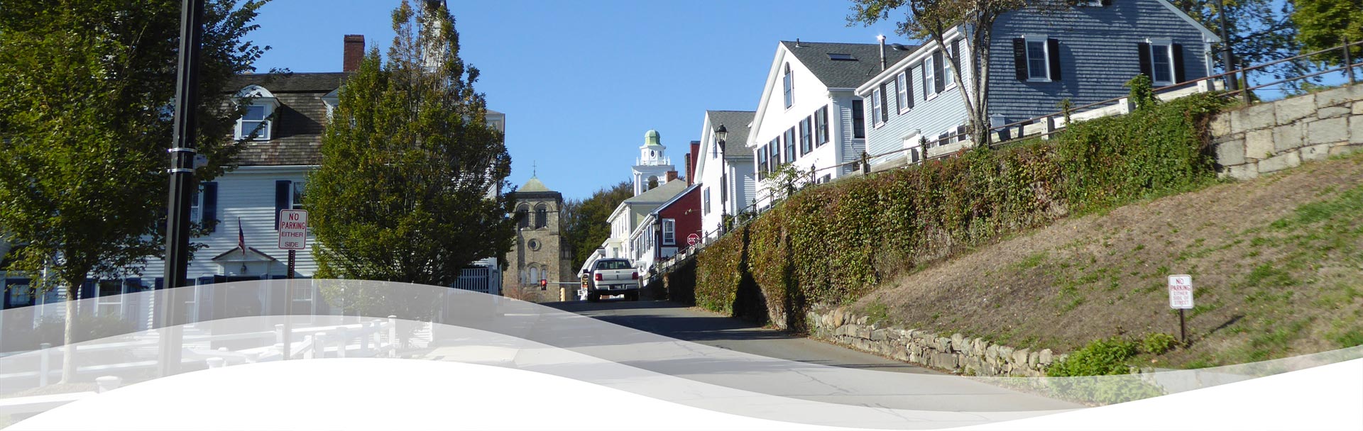 Sunny hillside street with historic homes and a church tower.