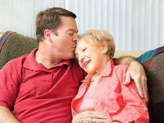 Son kissing elderly mother on head.