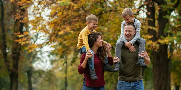 young family, mother and father with two young boys walking through an autumn forest