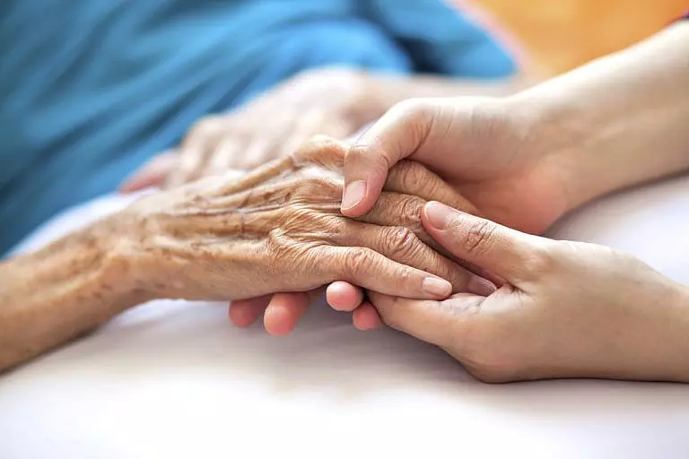 Elderly woman holding the hand of her personal representative.