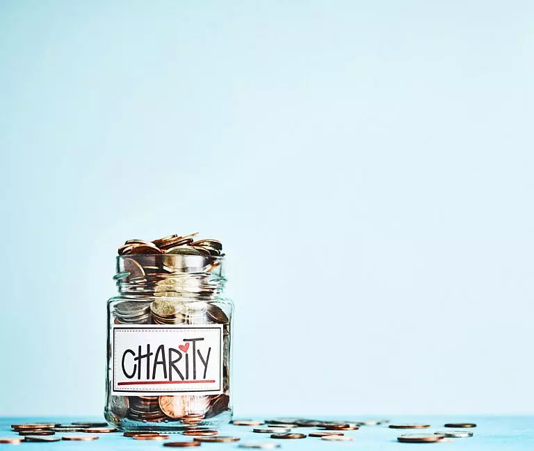 Jar of coins over blue background - representing charitable giving.