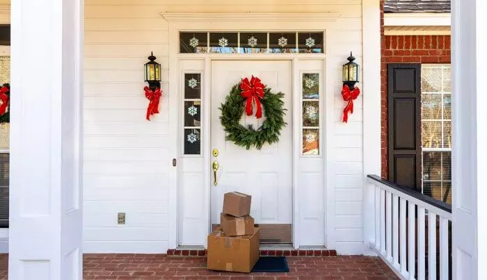 Boxes sitting on a **porch** in front of a **Christmas-decorated white door**.