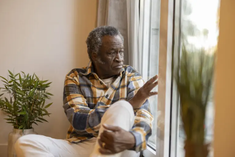 Elderly man sitting by a window looking sad