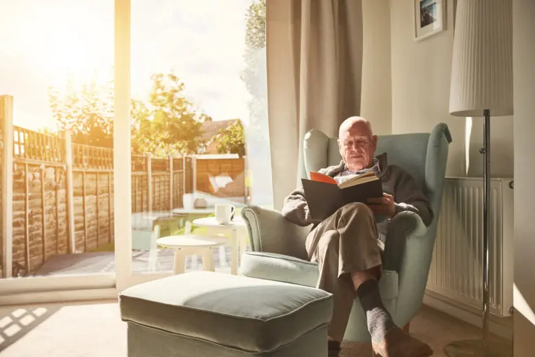 elderly man sitting in an armchair reading a book