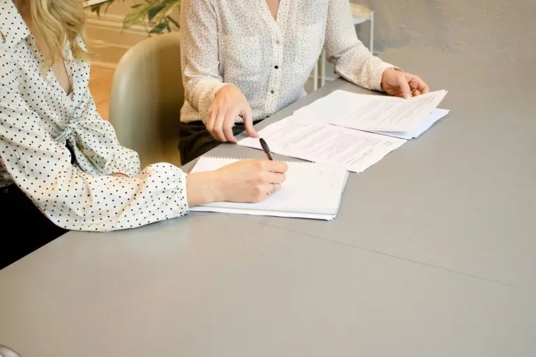 Two people reviewing and signing paperwork at a desk.