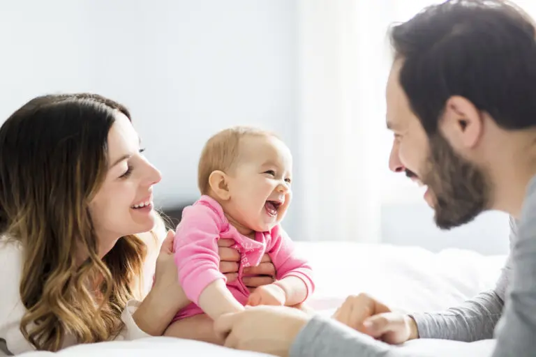 A Mother father and baby child on a white bed.