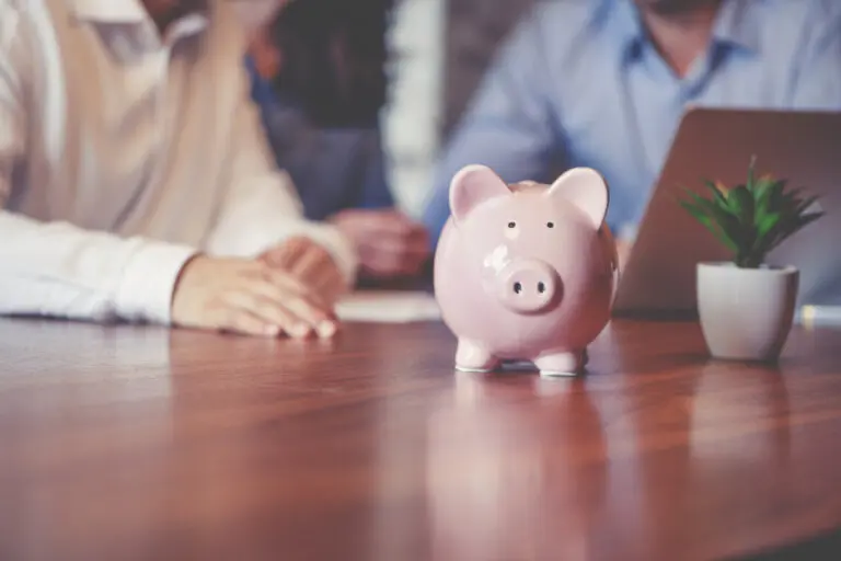 Pink piggy bank on a desk with a man and woman out of focus in the background