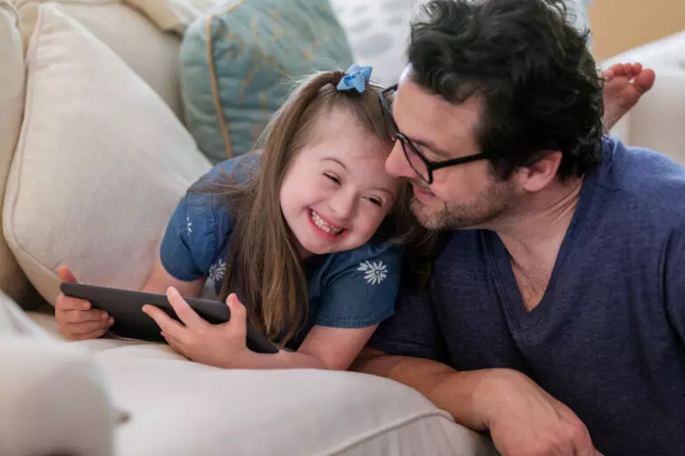 The young girl with Down Syndrome giggles with her mid adult father.